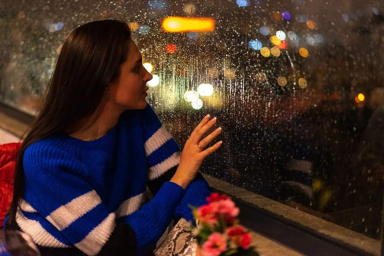 Raindrops streaking down a window with soft city lights in the background