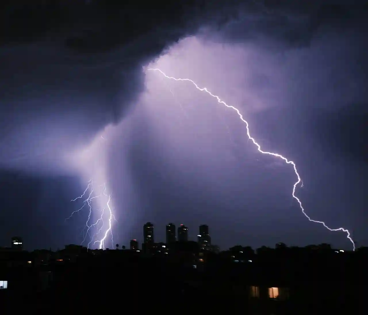 City storm at night — rain, wind and occasional lightning for a cinematic ambience Rain sweeping across a city at night with soft lightning illuminating the clouds