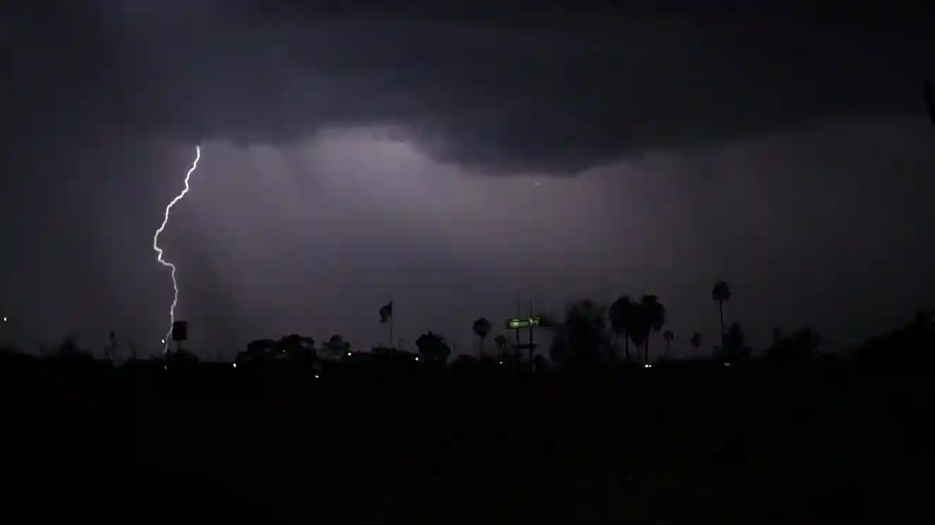 Dark storm clouds with rain and distant lightning over a quiet landscape